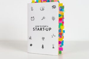 A book titled "How to Start a Start-Up" with numerous colorful sticky notes marking various pages, showcasing its extensive content. One of the best startup books for entrepreneurs looking to gain insights into launching a business.