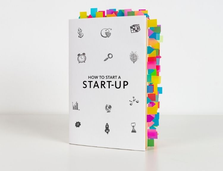 A book titled "How to Start a Start-Up" with numerous colorful sticky notes marking various pages, showcasing its extensive content. One of the best startup books for entrepreneurs looking to gain insights into launching a business.